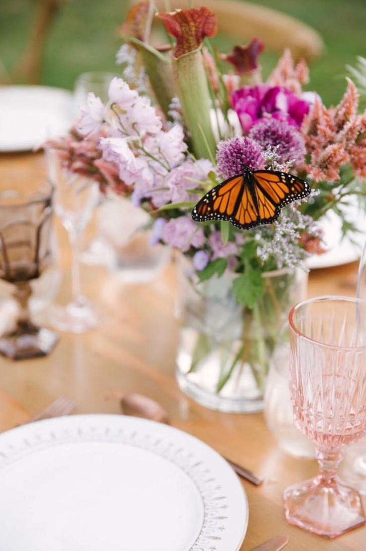 a vase filled with purple flowers sitting on top of a wooden table next to plates and glasses