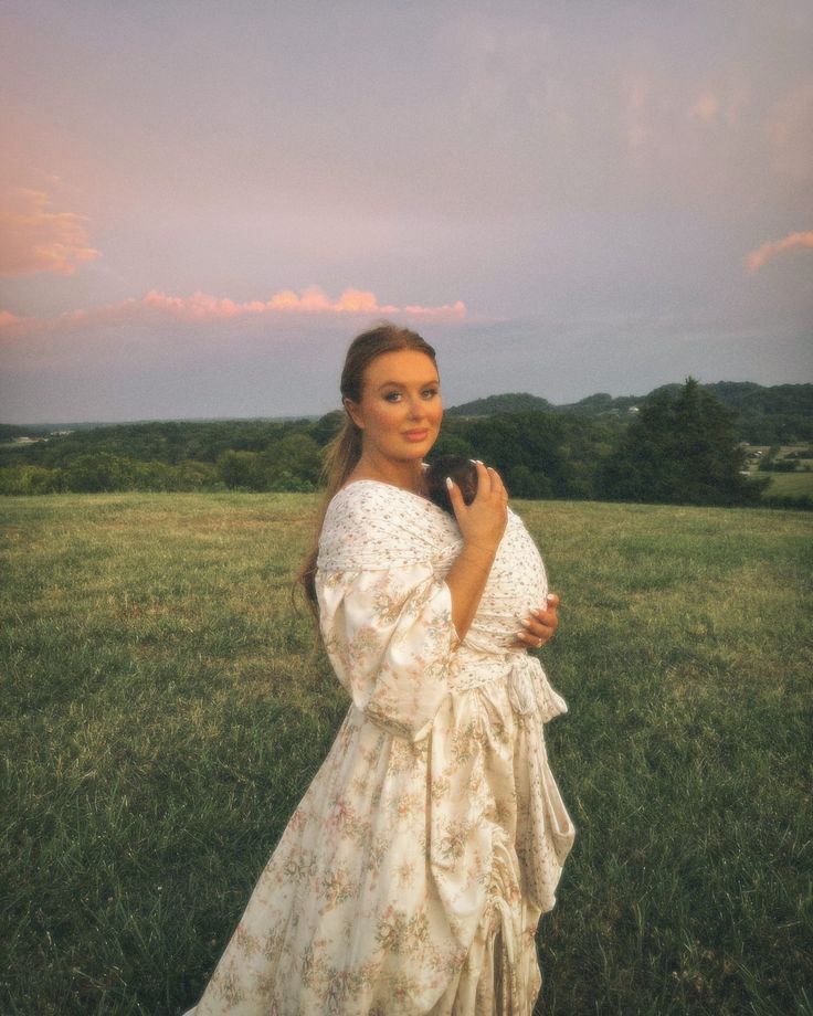 a woman in a white dress is standing in the grass with her hands on her chest