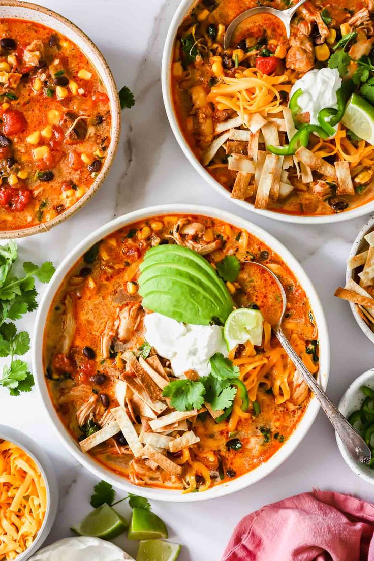 three bowls of mexican chicken soup with tortilla chips and avocado on the side