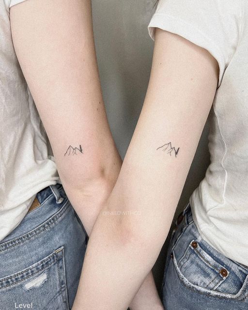 two women with matching tattoos on their arms, both holding each other's hands