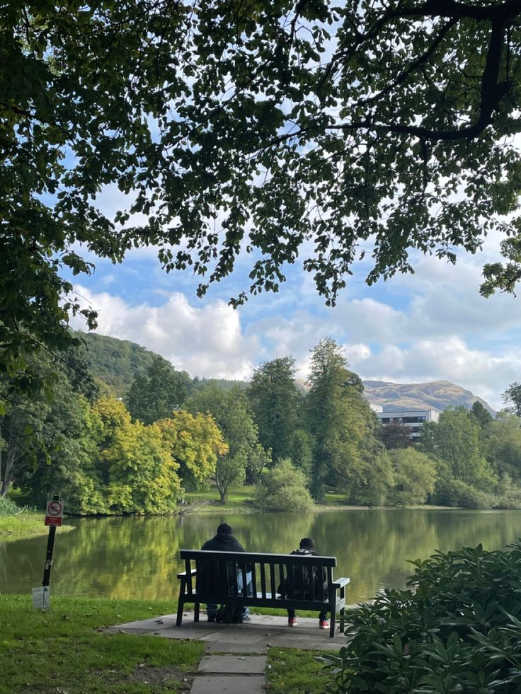 two people are sitting on a bench by the water