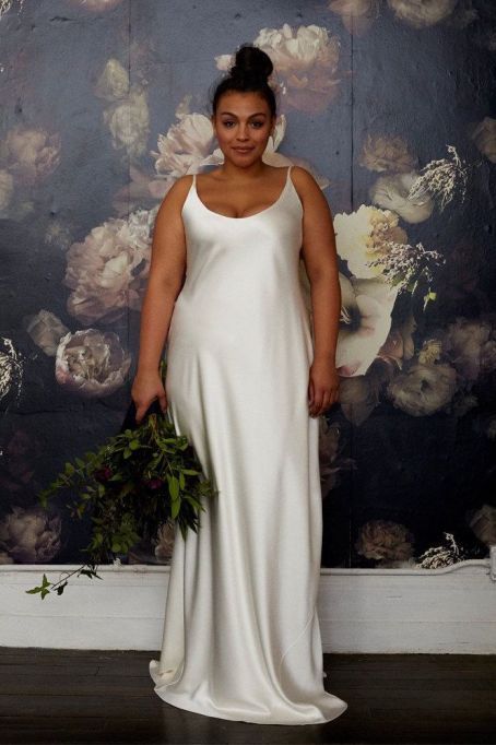 a woman standing in front of a floral wallpaper holding a flower bouquet and wearing a white dress