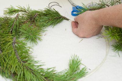 someone using scissors to trim a pine wreath