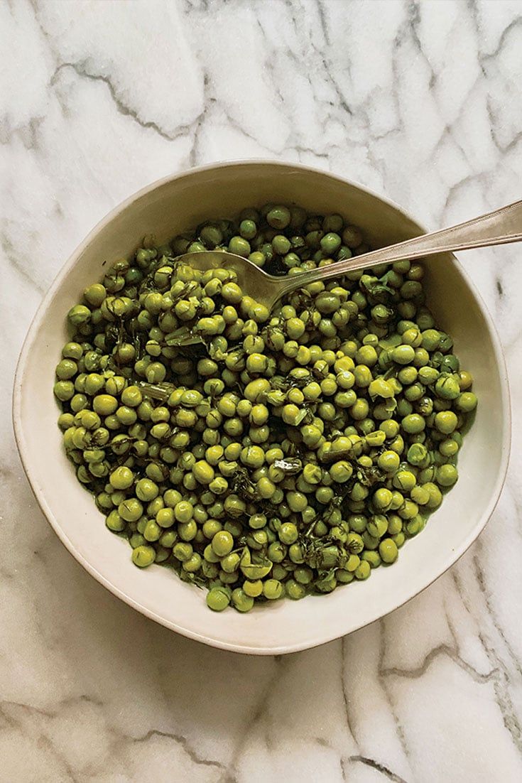 a white bowl filled with green peas on top of a marble counter next to a spoon