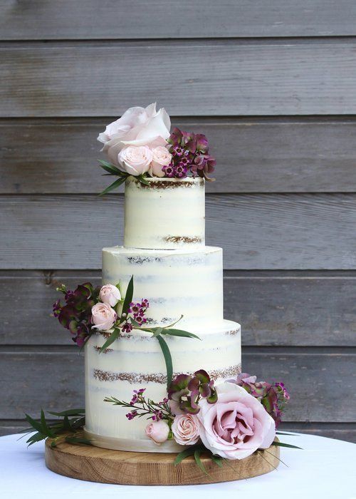 a three tiered wedding cake with pink flowers on top and greenery around the edges