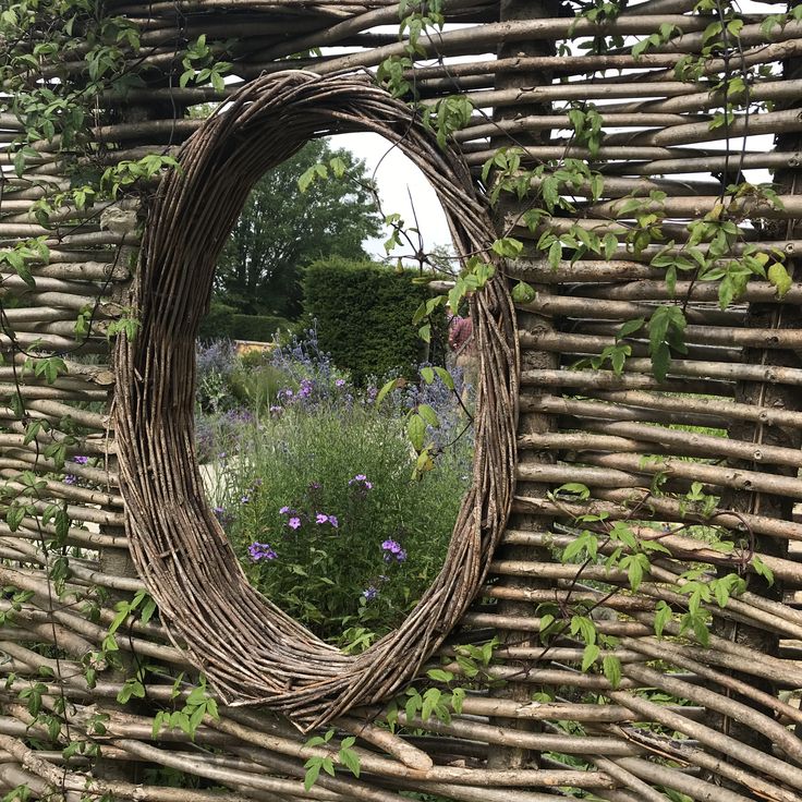 a circular mirror sitting on the side of a wall covered in vines and flowers next to a garden