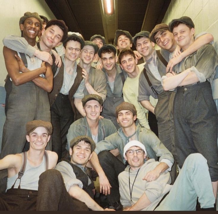 a group of young men standing next to each other in front of a wall with their arms around each other