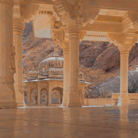 an ornate building with pillars and arches in front of a mountain range, surrounded by trees