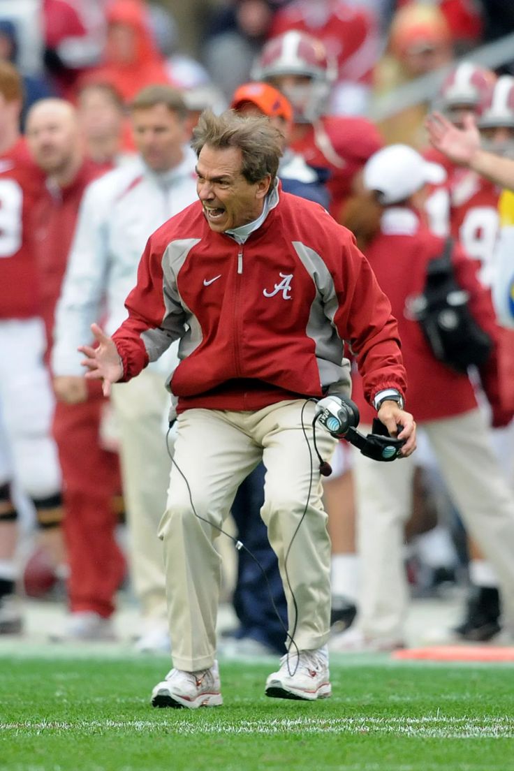 a man in a red jacket and white pants on the sidelines with his hands out