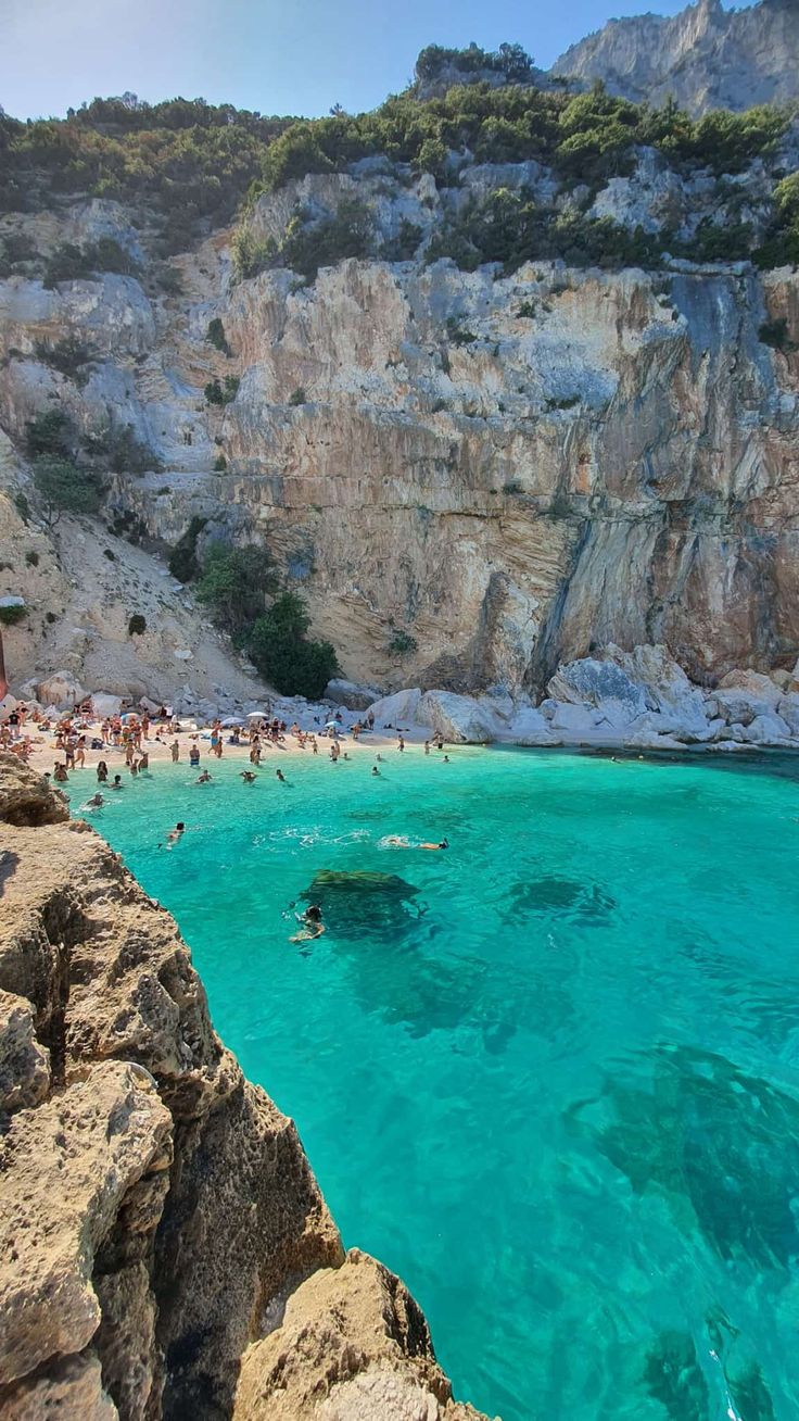 people are swimming in the clear blue water near some rocky cliffs and cliffs,