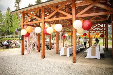 an outdoor wedding venue with tables and white tablecloths, red and yellow lanterns hanging from the ceiling