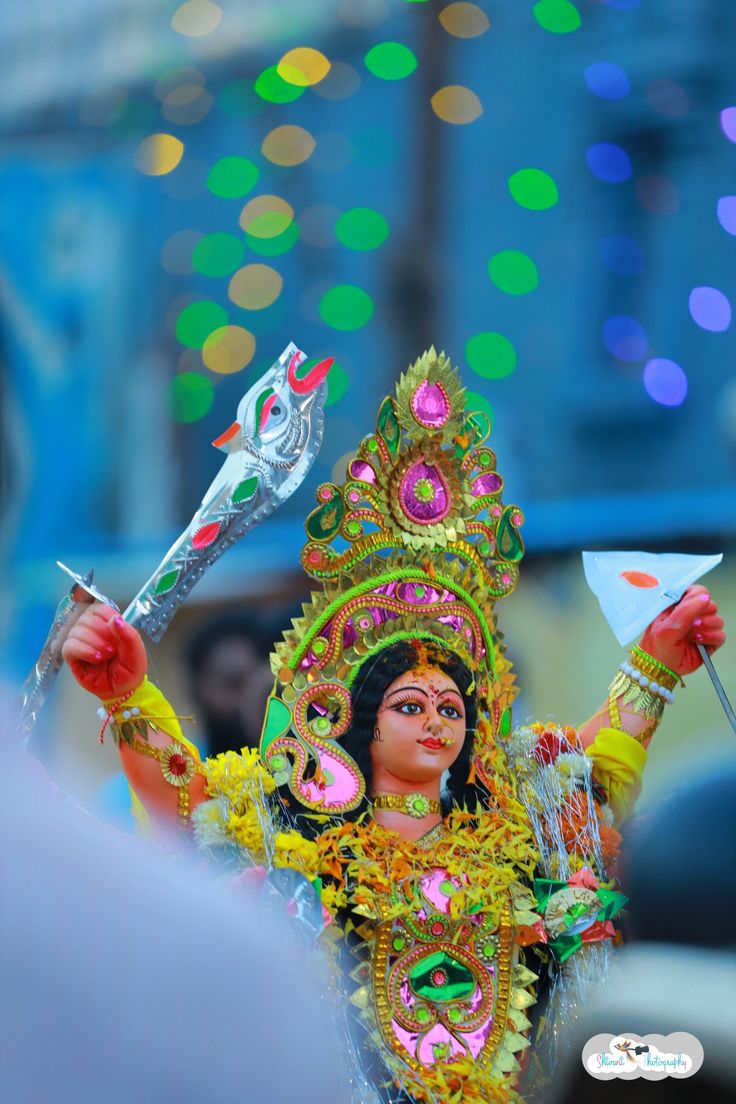 a woman dressed in an elaborate costume and holding a small item on her head with lights behind her