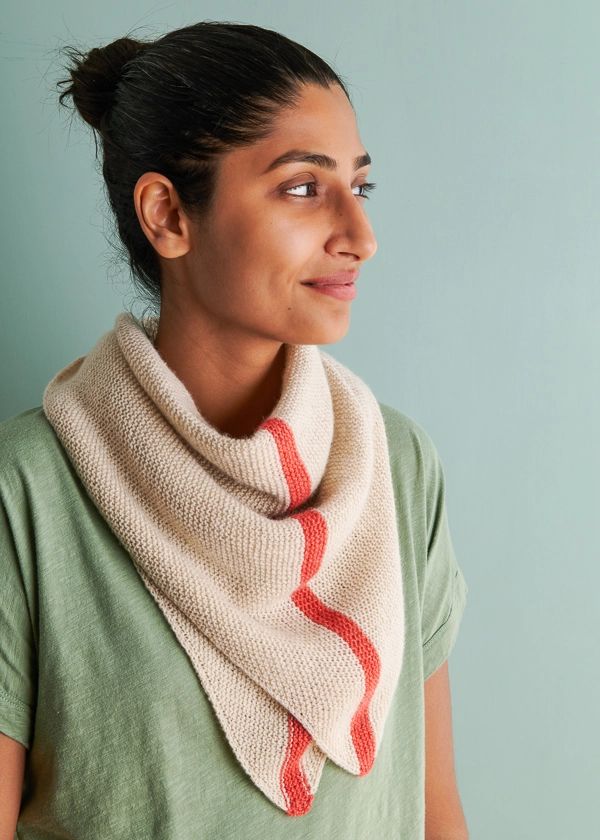 a woman wearing a knitted scarf with red and white stripes on the bottom, standing in front of a blue wall