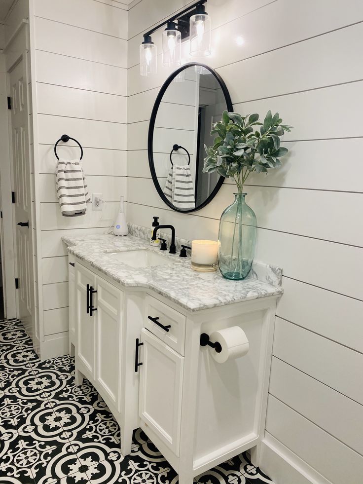 a white bathroom with black and white flooring, two sinks and a large round mirror on the wall