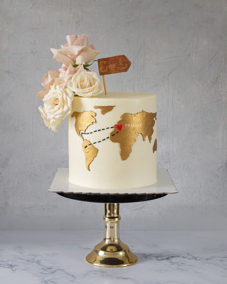 a white and gold wedding cake with flowers on the top is decorated with a world map