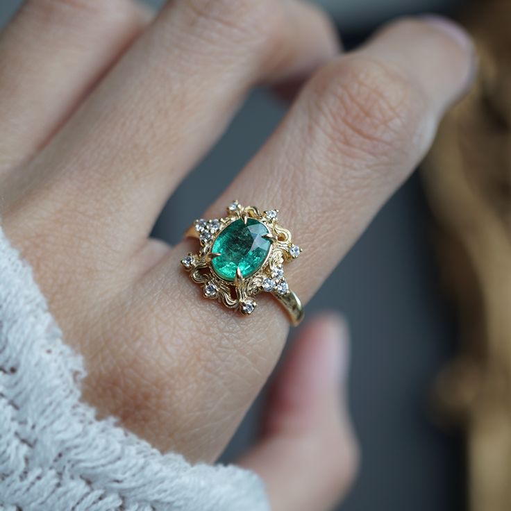 a close up of a person's hand wearing a ring with an emerald stone