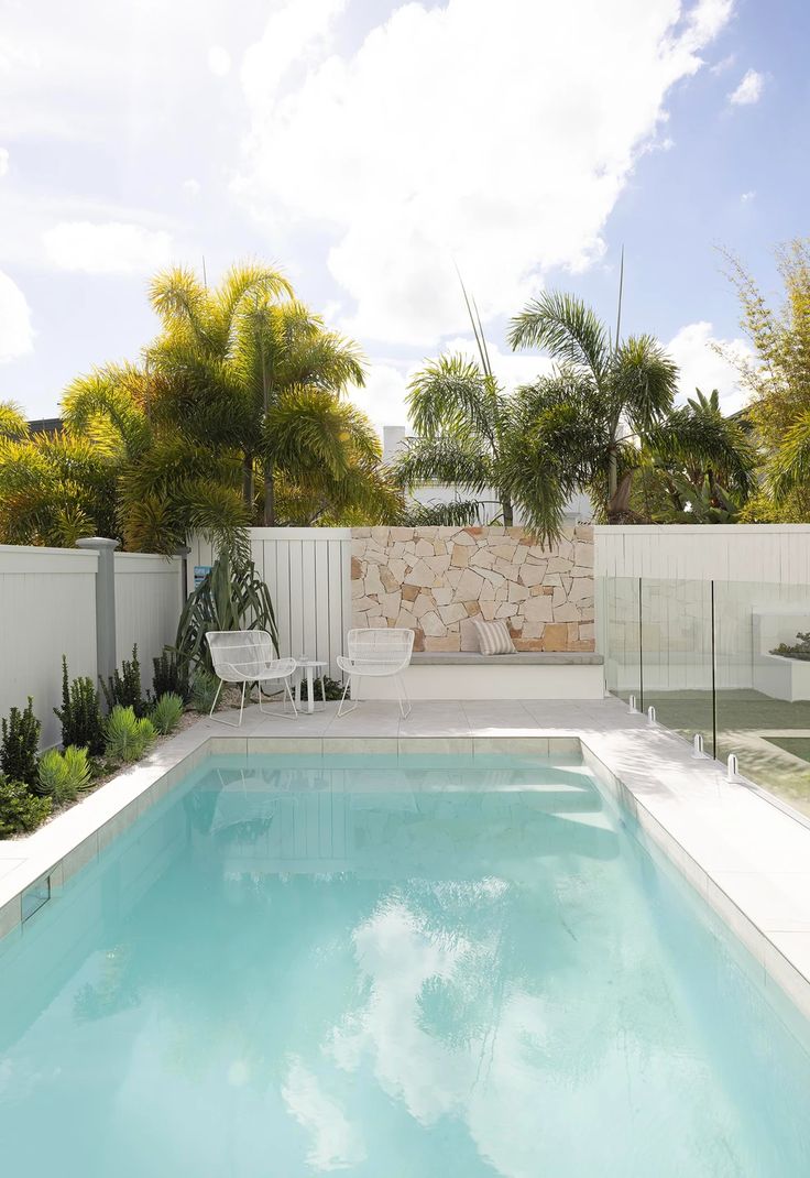 an empty swimming pool in the middle of a tropical garden with white fence and palm trees