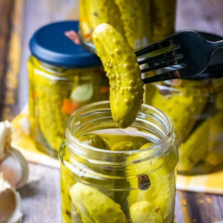 pickles are being lifted from a jar by a fork with garlic on the side