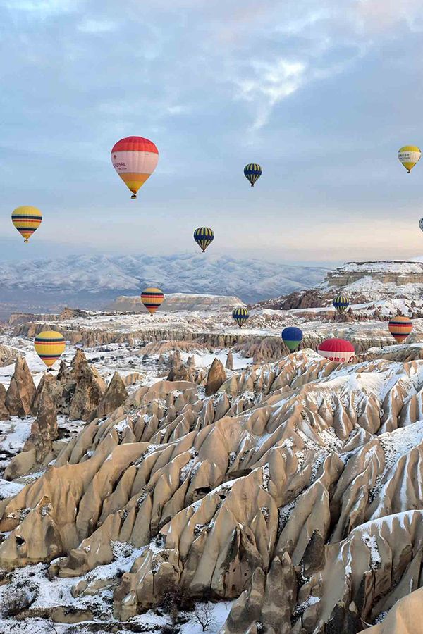 many hot air balloons are flying in the sky over some snow covered rocks and mountains