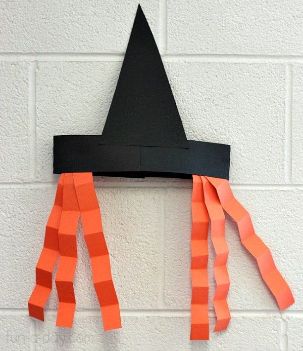 an orange and black paper hat hanging on a wall with strips of tape attached to it