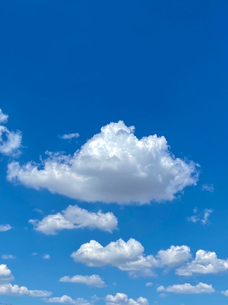 an airplane flying in the blue sky with white clouds and some grass on the ground