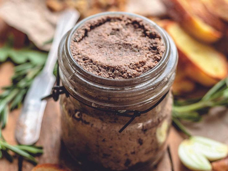 a jar filled with brown stuff sitting on top of a wooden table next to sliced apples