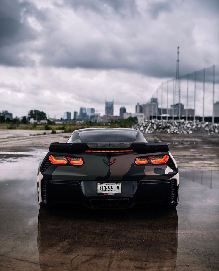 the rear end of a black sports car parked in front of a cityscape