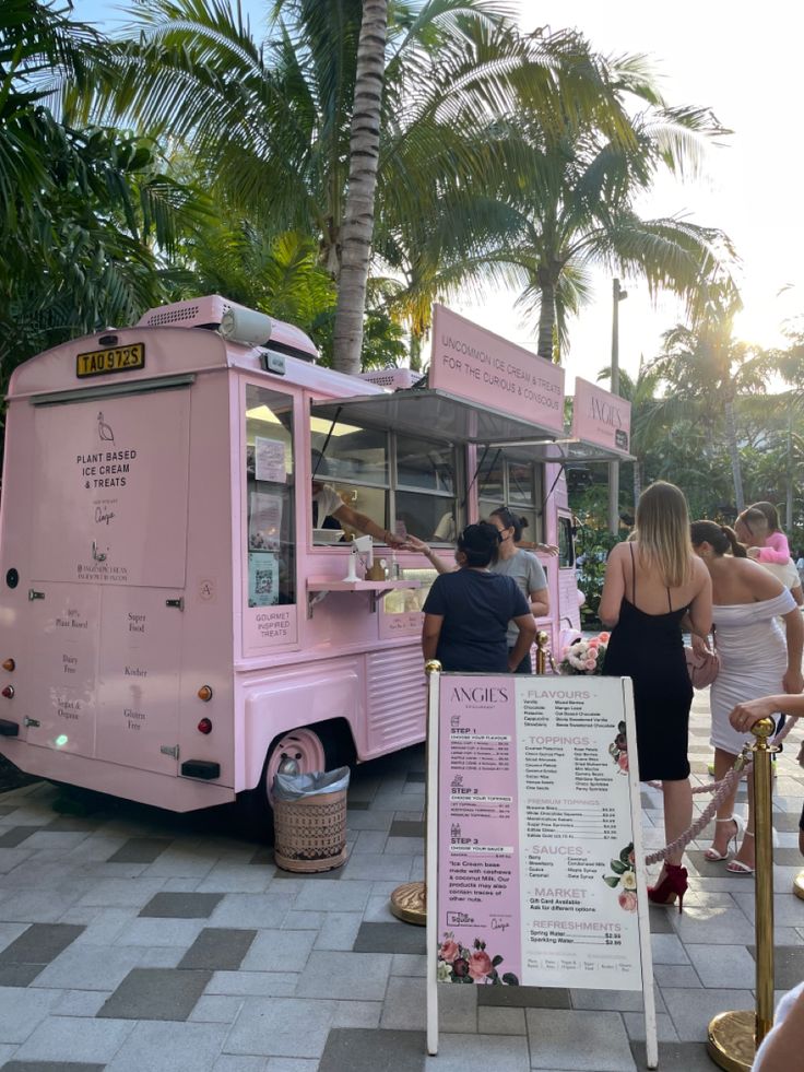 a pink food truck parked next to a palm tree