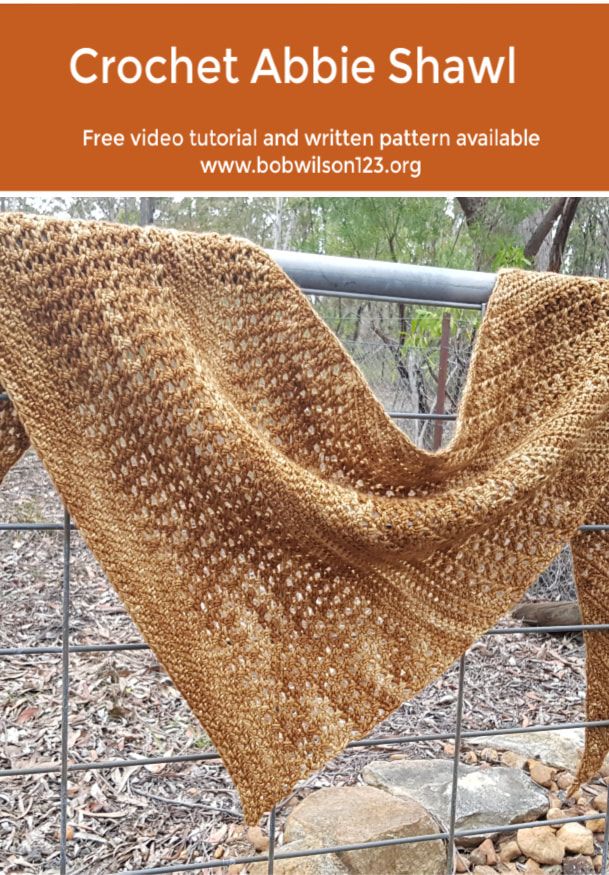 a knitted shawl sitting on top of a fence next to rocks and trees