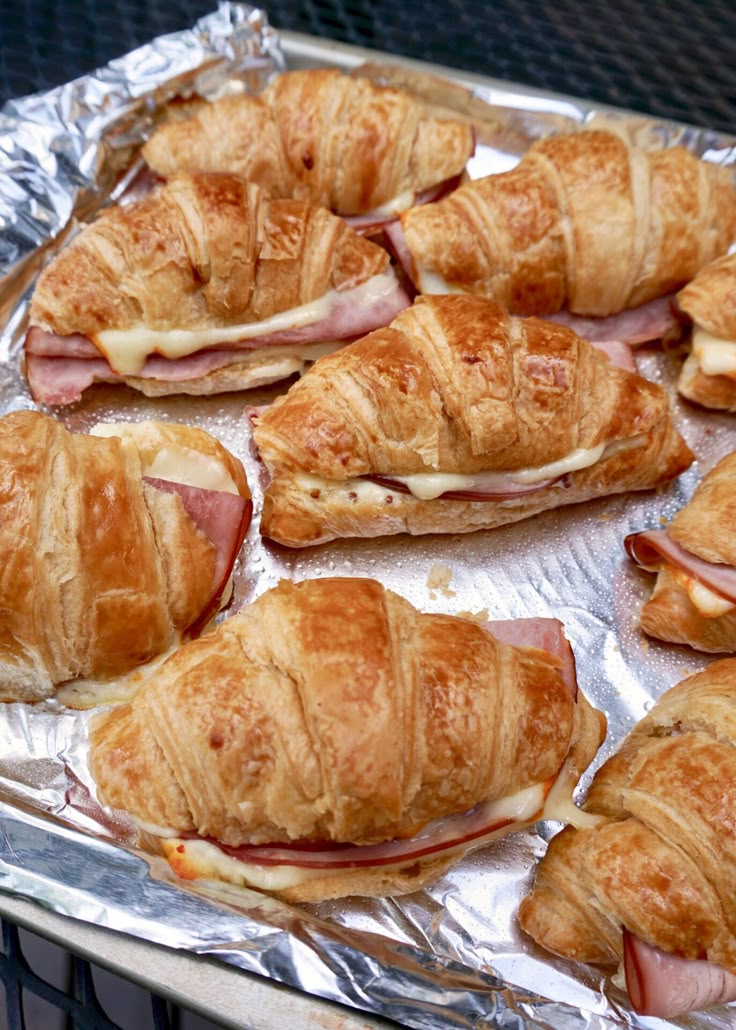 several croissants with ham and cheese on them sitting on tinfoil covered baking sheet