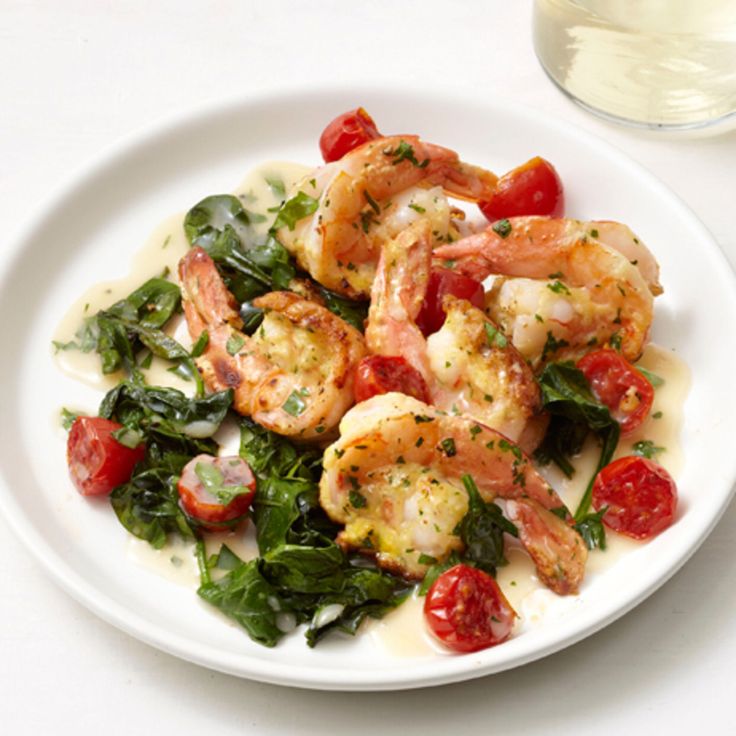 a white plate topped with shrimp and spinach next to a glass of water