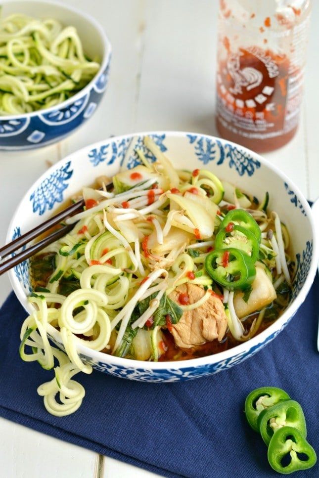 a bowl filled with noodles and vegetables on top of a blue napkin next to chopsticks