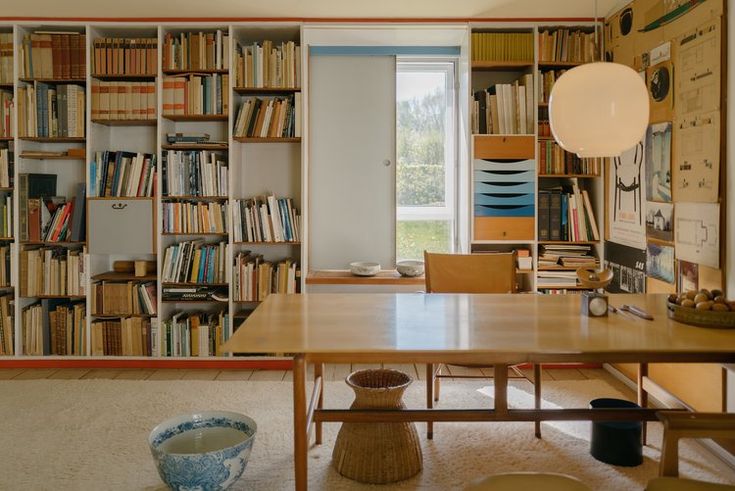 a room filled with lots of books on shelves next to a table and chair in front of a window