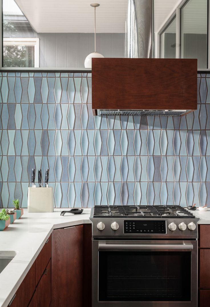 a kitchen with wooden cabinets and stainless steel stove top oven in front of a blue tile backsplash