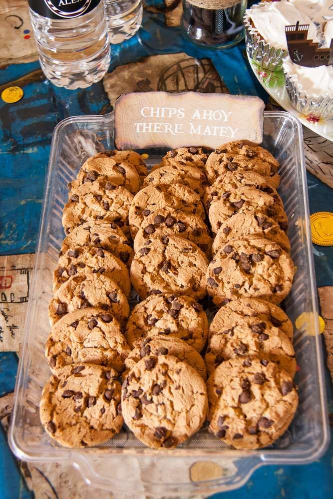 chocolate chip cookies in a plastic container on a table with water glasses and other items