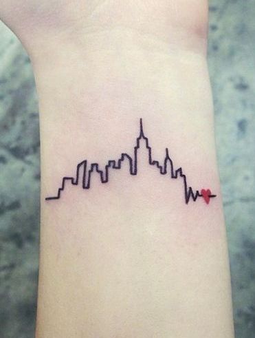 a small wrist tattoo with an arrow in the shape of a cityscape on it