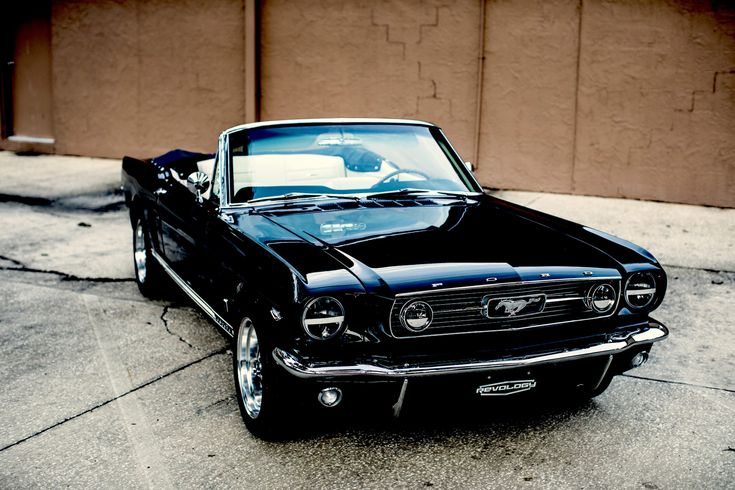 an old black mustang parked in front of a building