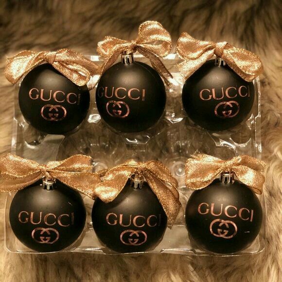 four black and gold christmas ornaments in a clear box with bows on the top one is for gucci