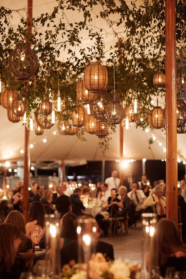 many people are sitting at tables with lights hanging from the ceiling and greenery over them