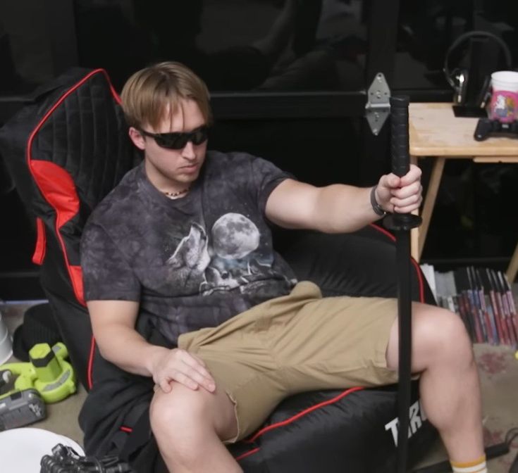 a young man sitting in a chair holding a large knife and looking at the camera