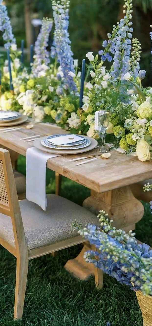 a long table with blue and white flowers on it is set up for an outdoor dinner