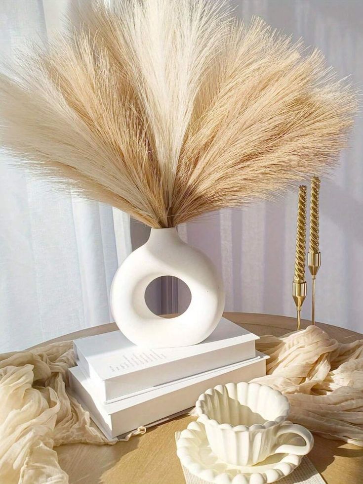 a vase with some dry grass in it on a table next to a book and cup