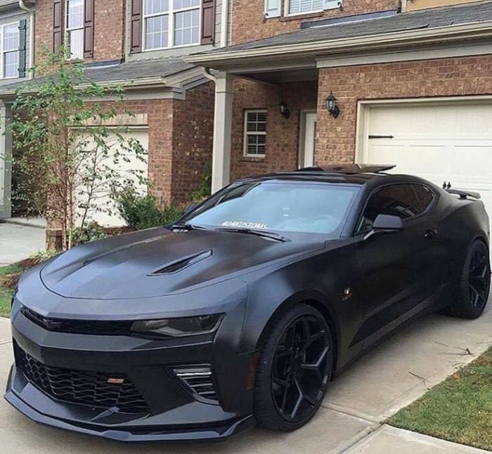 a black chevrolet camaro is parked in front of a house with the word kaji written on it