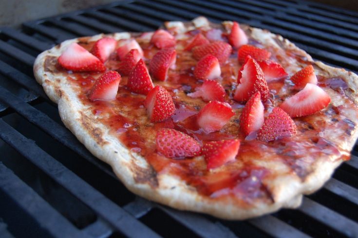 a pizza sitting on top of a grill covered in lots of toppings and sliced strawberries