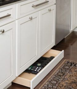 a kitchen with white cabinets and drawers has an open drawer in the middle that holds a remote control