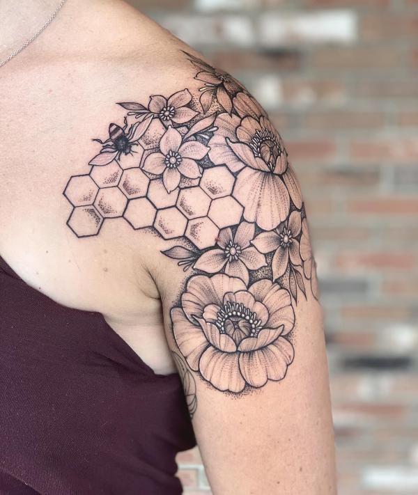 a woman's shoulder with flowers and honeycombs tattooed on her left arm