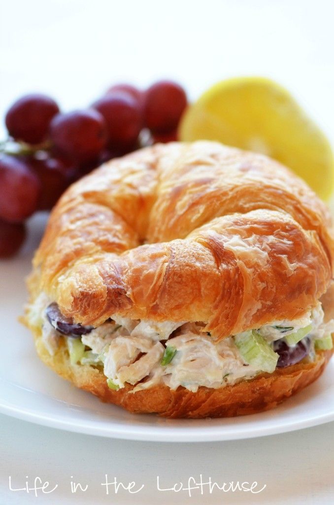 a croissant sandwich with chicken salad on it next to grapes and lemons