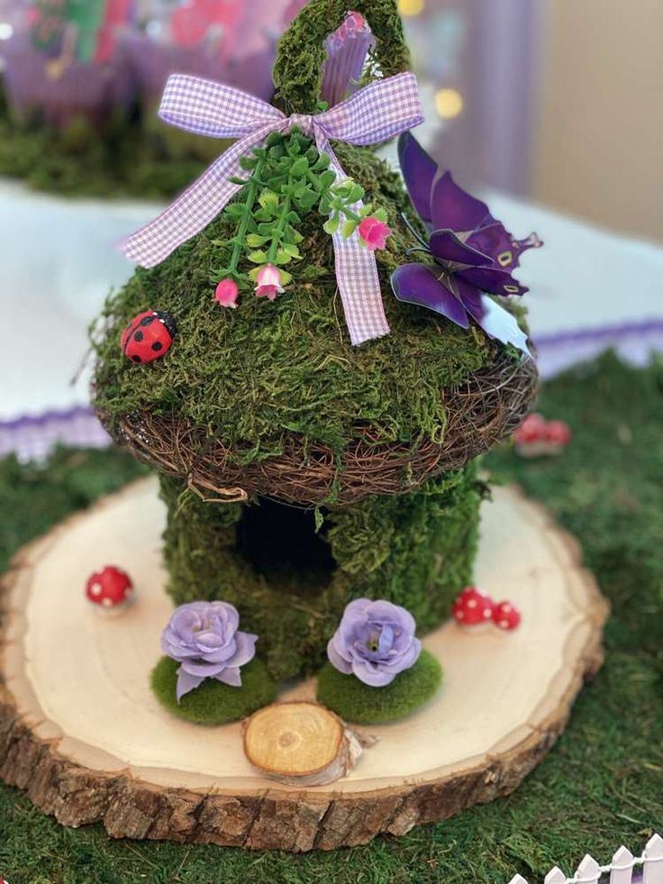 a small house made out of moss with purple flowers and ladybugs on it