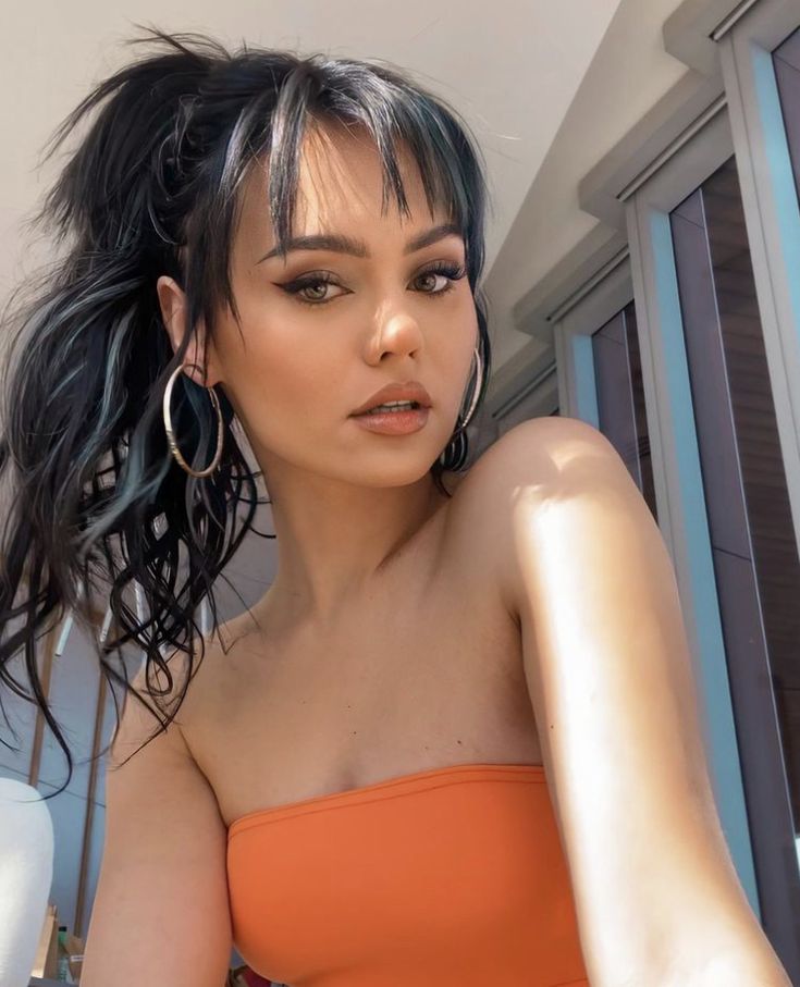 a close up of a person wearing an orange dress and large hoop earrings with her hair blowing in the wind