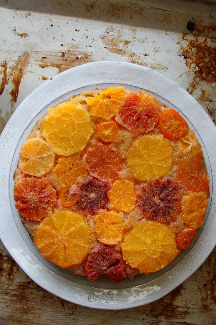 an orange and raspberry upside down cake on a white plate with rusted surface